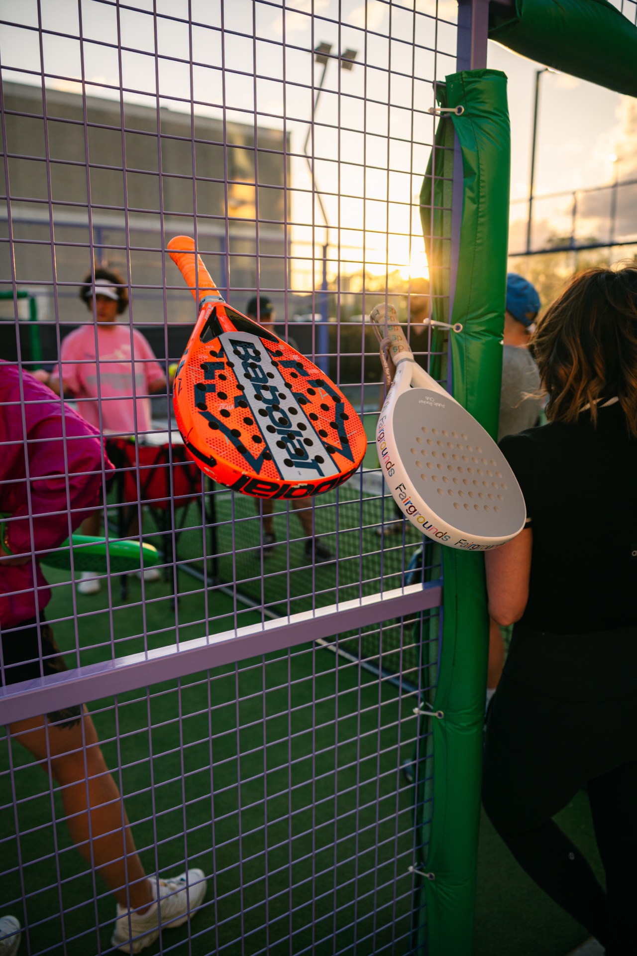 Paddles hooked on the court fence at golden hour